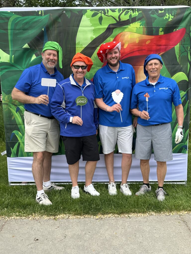 Four Centennial Homes team members in blue shirts and fun hats at a charity golf tournament